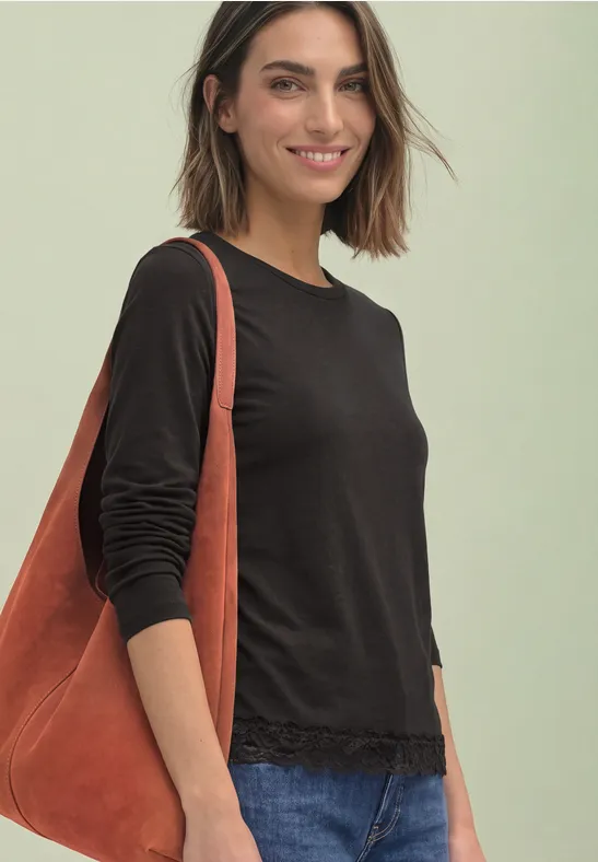 Frau mit schulterlangem braunem Haar, schwarzem Shirt und orangefarbener Tasche lächelnd vor hellem Hintergrund.