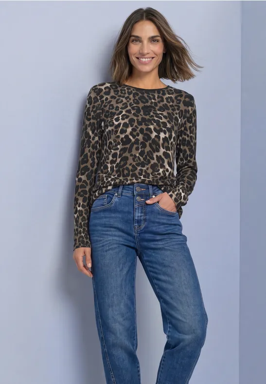 Frau trägt Leoparden-Print-Pullover und blaue Jeans vor neutralem Hintergrund.