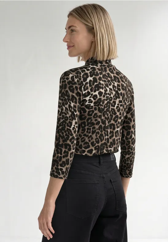 Frau in leo-Longsleeve mit Rollkragen und schwarzer Hose, Seitenansicht nach links.