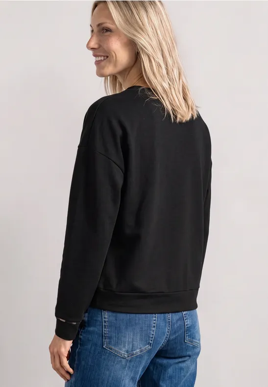 Femme de profil portant un pull noir et un jean bleu.