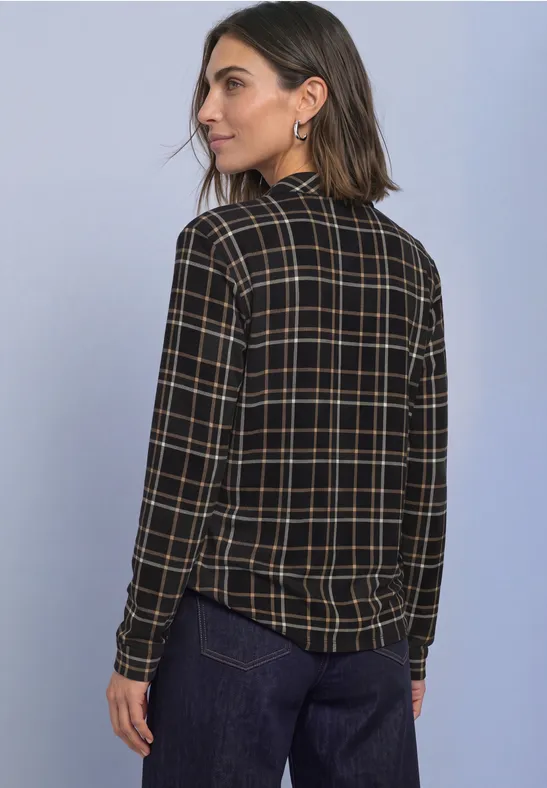 Femme porte chemise à carreaux manches longues et pantalon sombre, regarde par-dessus l'épaule.