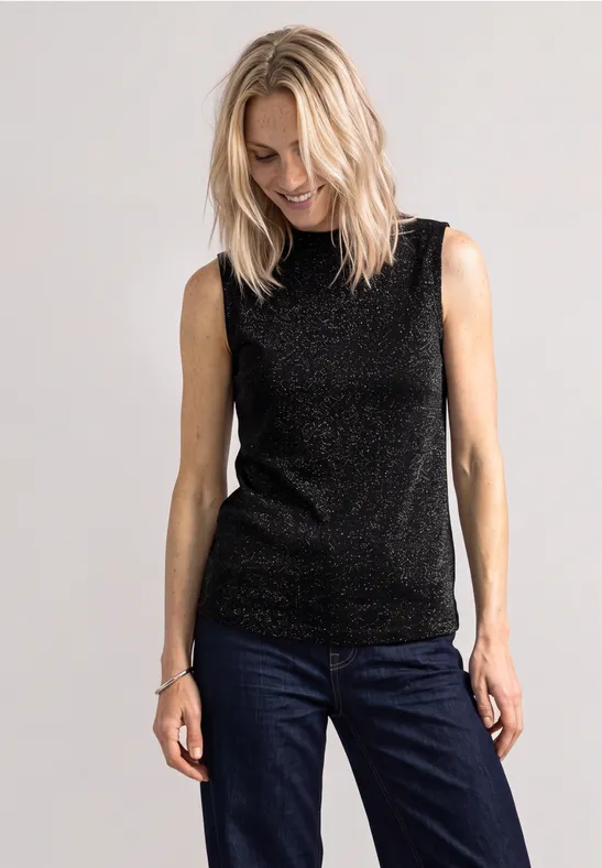 Eine Frau trägt ein schwarzes Glitzer-Top und blaue Jeans.