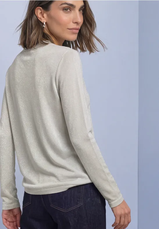 Frau von hinten in hellem Langarmshirt und dunkler Jeans, Blick über die Schulter.