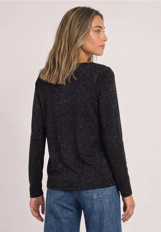 Vrouw van achteren met zwarte glanzende top en blauwe spijkerbroek tegen lichte achtergrond.