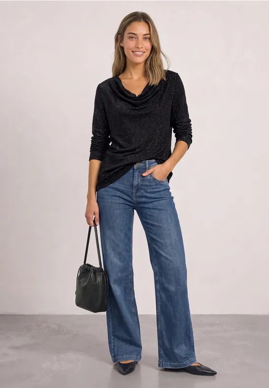 Vrouw in zwarte coltrui met watervalhals, wijde blauwe jeans, puntige flats en zwarte leren tas.