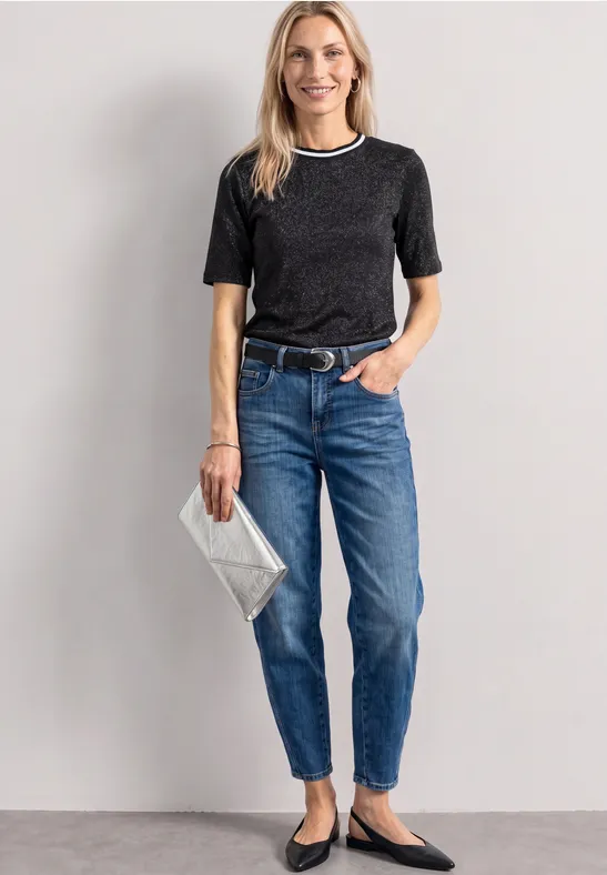 Eine Frau in schwarzem Kurzarmshirt mit weißem Rand und blauen Jeans, hält eine silberne Clutch.
