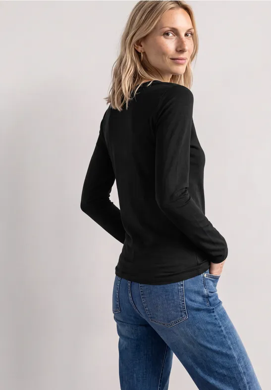 Femme portant un haut noir à manches longues et un jean bleu, vue de profil, regard par-dessus l’épaule.