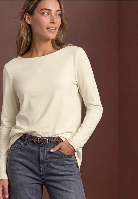 Een vrouw in een crèmekleurige longsleeve en jeans, casual pose.