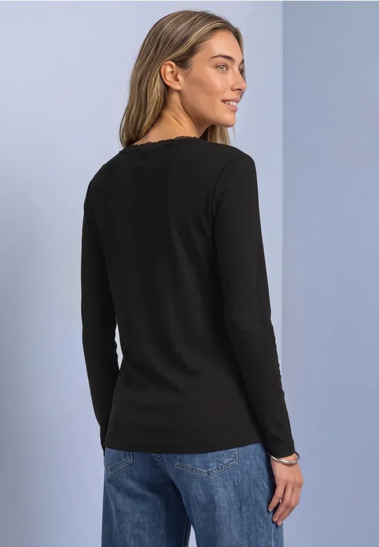 Profilaufnahme einer Frau in schwarzem Langarmshirt und blauen Jeans.