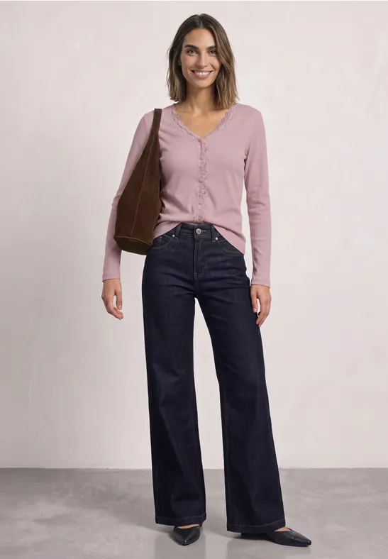 Frau trägt rosa Cardigan, dunkelblaue Schlagjeans und hält eine braune Tasche.