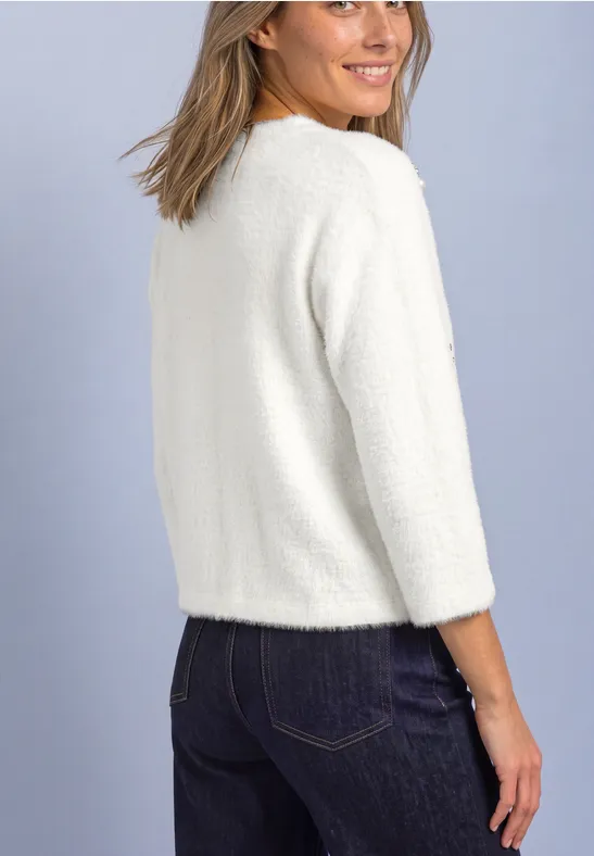 Eine Frau von hinten in einem weißen Pullover und dunklen Jeans, die über die Schulter lächelt.
