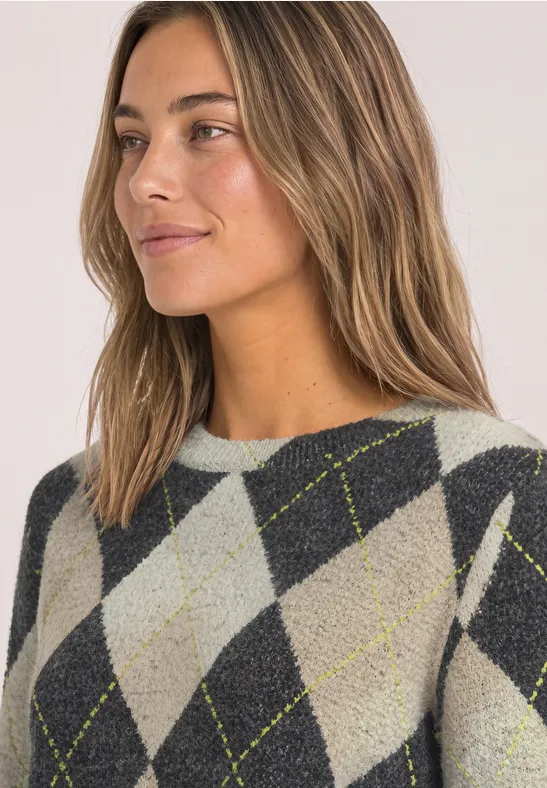 Frau mit leicht gewelltem hellbraunem Haar in grauem Argyle-Pullover mit gelben Linien.