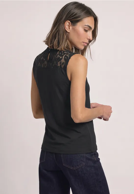 Frau von hinten in ärmellosem schwarzen Spitzen-Top und dunkler Jeans.