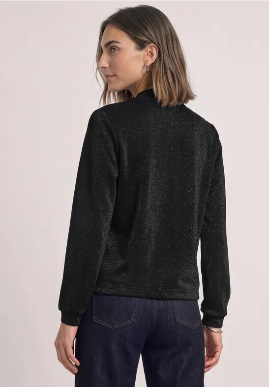 Frau von hinten in funkelndem schwarzen Pullover und blauer Jeans vor hellem Hintergrund