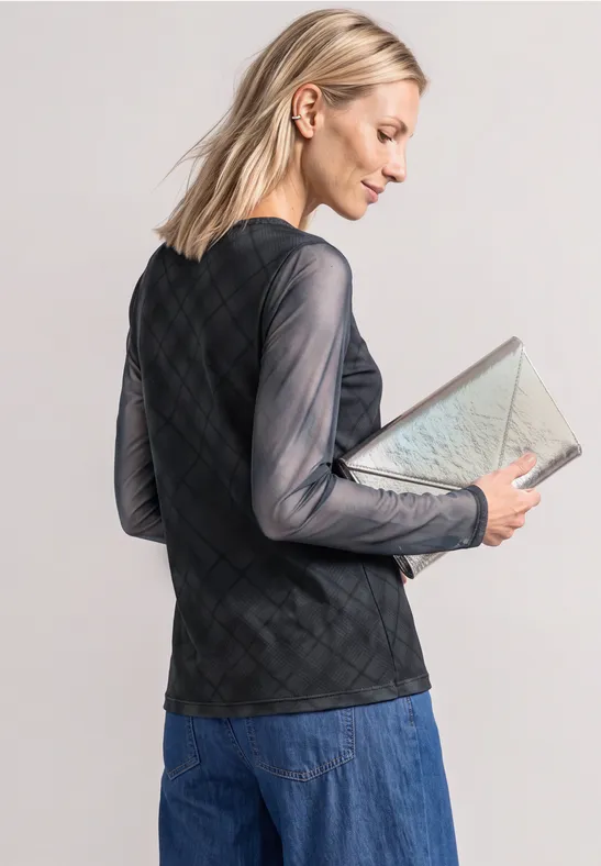 Frau mit blonden Haaren in schwarzem, transparentem Rautentop und Jeansrock hält beige Clutch.