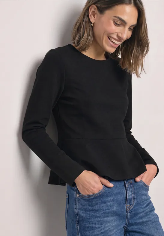 Eine lächelnde Frau in schwarzem Pullover und Jeans schaut seitlich nach unten.
