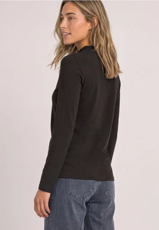 Eine junge Frau im Profil, trägt schwarzen Pullover und blaue Jeans, Blick über die Schulter.