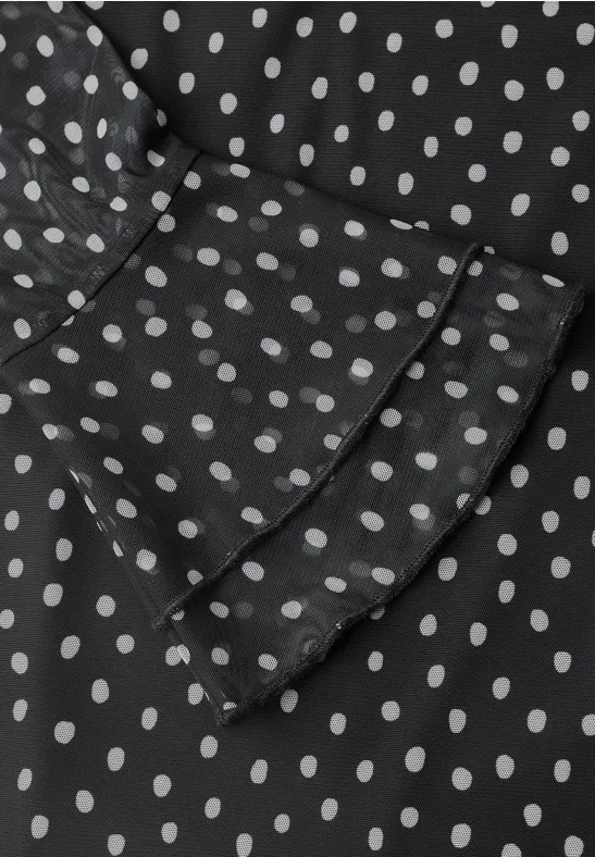 Schwarzer Stoff mit weißen Polka Dots und Rüschen am Ärmel.