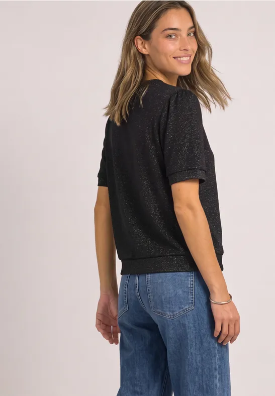 Eine lächelnde junge Frau in schwarzem T-Shirt und blauen Jeans blickt über die Schulter.