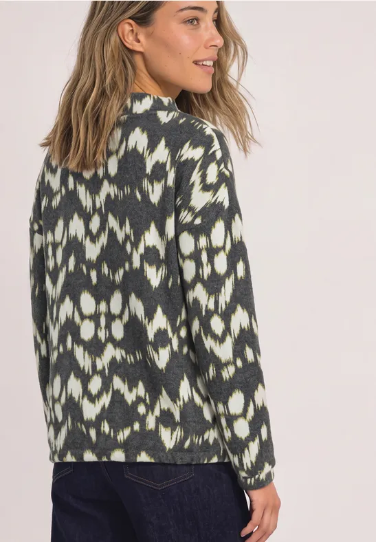 Eine Frau trägt einen Pullover mit grün-weißem Ikat-Muster und schaut über die Schulter.