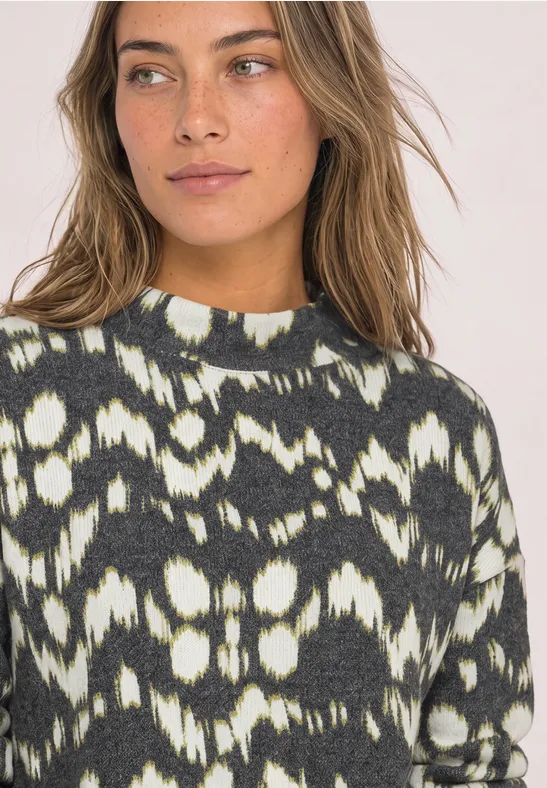 Eine Frau trägt einen schwarz-weißen Pullover mit abstraktem Muster, blickt seitlich.