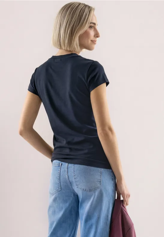 Junge Frau in schwarzem T-Shirt und hellblauer Jeans, hält eine bordeauxrote Tasche, Ansicht von hinten.