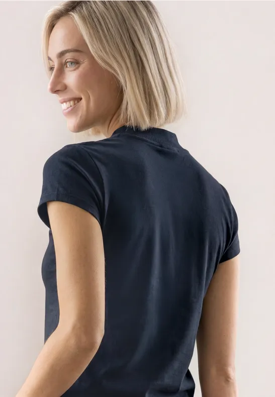 Lächelnde blonde Frau in schwarzem T-Shirt, seitlich gesehen.