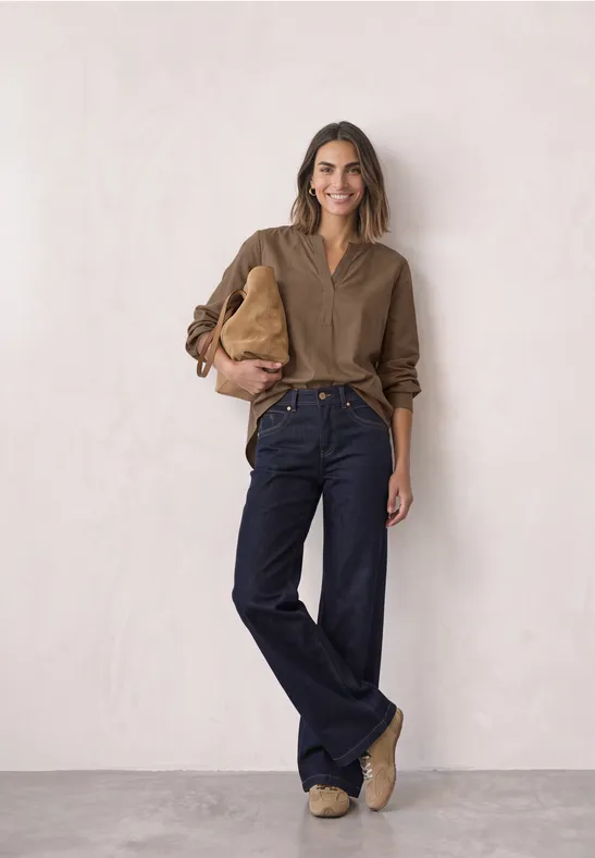 Frau in legerem Outfit mit weiten Jeans, braunem Hemd und Tasche.