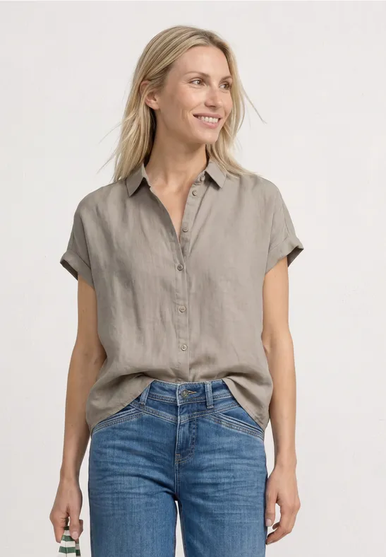 Eine Frau trägt eine kurzärmlige graue Leinenbluse und blaue Jeans.