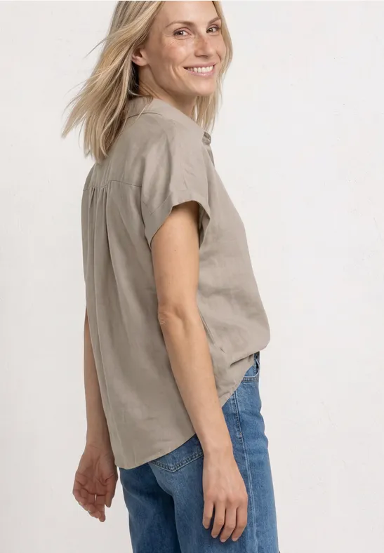 Seitlich aufgenommene Frau trägt beige Hemdbluse und blaue Jeans.