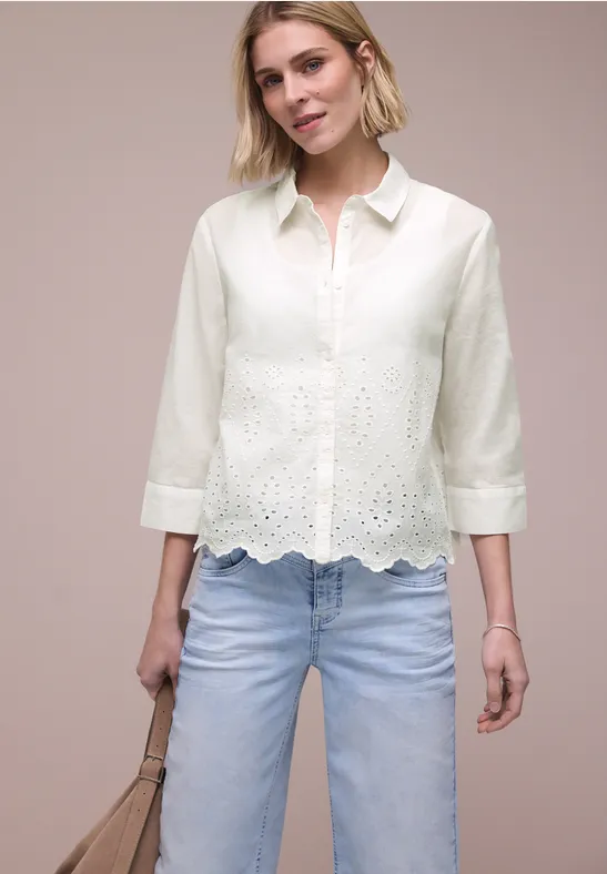 Vrouw in witte geborduurde blouse met 3/4-mouwen en lichte jeans, met een beige tas.
