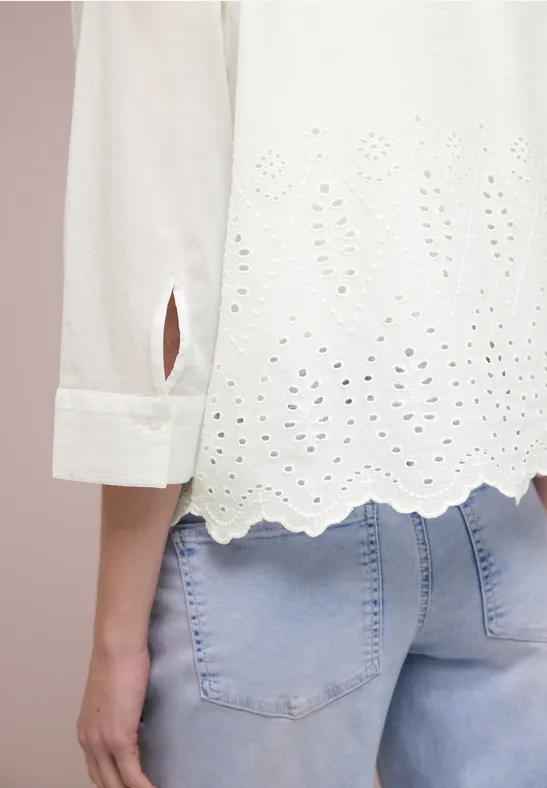 Witte blouse met borduursel en geschulpte zoom, gecombineerd met een lichtblauwe jeans.