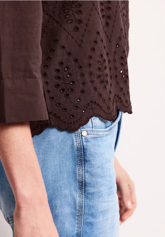 Vue latérale d'une personne en jean bleu clair et haut marron ajouré à ourlet festonné.