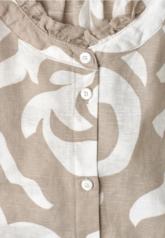 Close-up van een beige-witte blouse met bloemmotief en witte knopen.