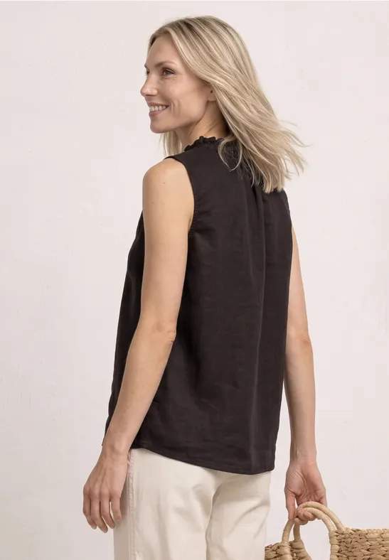 Frau von hinten in schwarzem ärmellosem Top und hellen Hosen, trägt einen Strohkörbchen, blonde Haare.