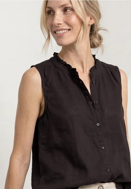 Frau in ärmelloser schwarzer Bluse mit geknöpftem V-Ausschnitt und Rüschen, lächelnd.