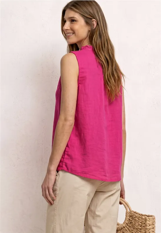 Frau von hinten mit pinkem ärmellosem Top, hellen Hosen und Basttasche vor neutralem Hintergrund.