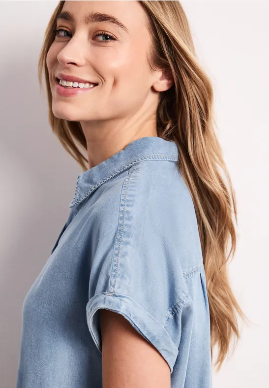 Zijaanzicht van een persoon met lang haar en een lichtblauw spijkerblouse met opgerolde mouwen