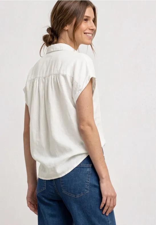 Persoon van achteren met wit kort mouw overhemd en blauwe jeans, haar losjes in een knot.