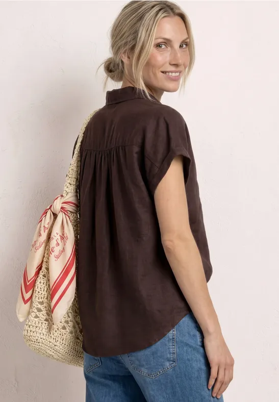 Femme de dos en chemisette marron et jean, portant un sac en paille et un foulard rouge et blanc.