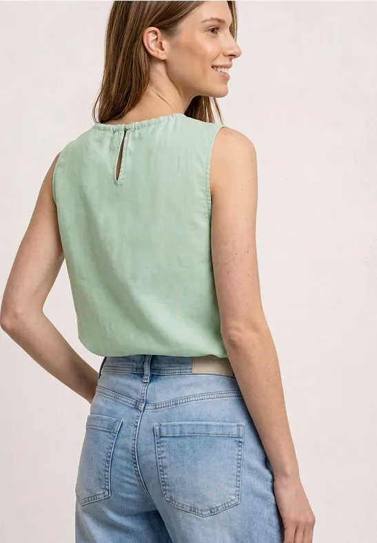 Eine Frau von hinten trägt ein ärmelloses mintgrünes Top und helle Jeans.