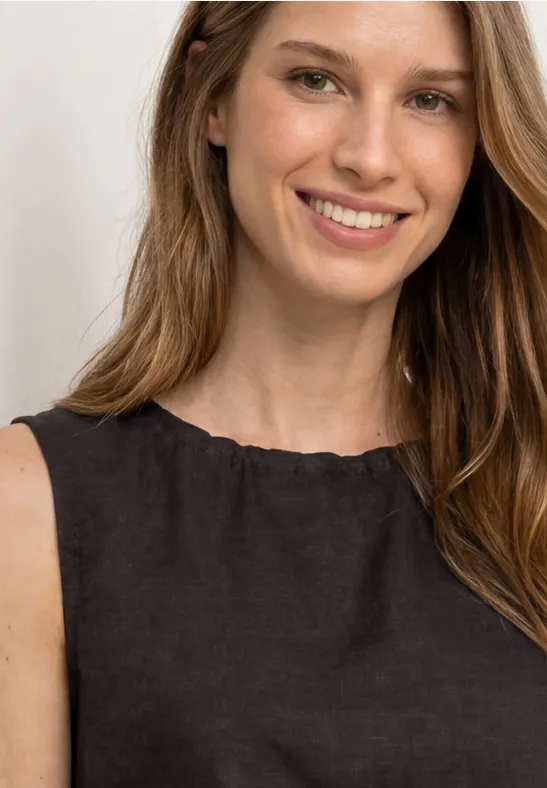 Eine Frau mit langem hellbraunem Haar trägt ein schwarzes ärmelloses Oberteil. Gesicht unscharf.