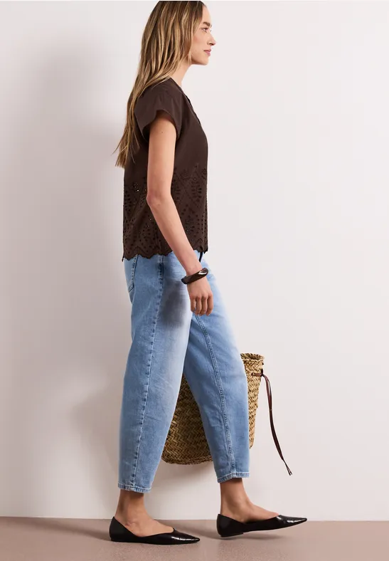 Vue latérale d'une femme en jean, haut noir, ballerines et sac en paille.