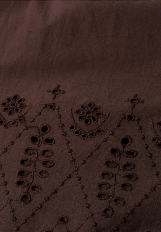 Gros plan d’un tissu brun foncé orné de broderies florales et de motifs en forme de feuilles.