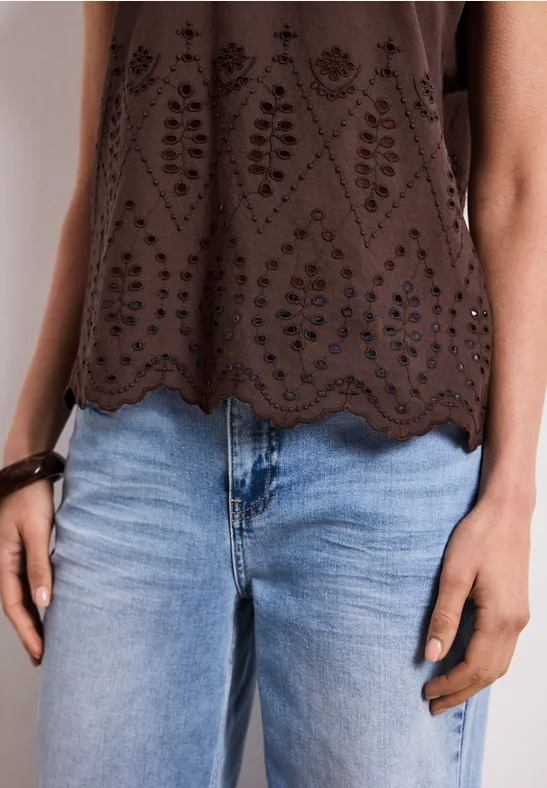 Une personne porte un haut brun ajouré et un jean bleu clair.