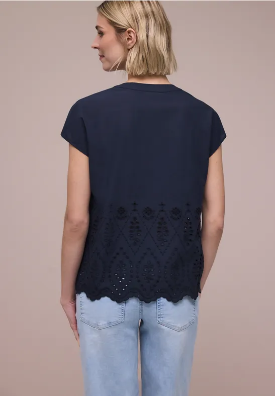 Vrouw van achteren in donkerblauw kort shirt met kantachtige onderrand en lichte spijkerbroek.