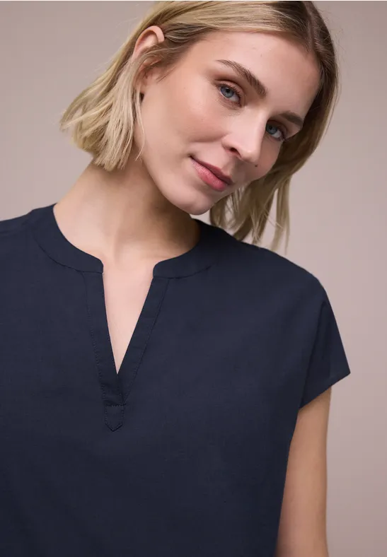 Persoon met blond haar draagt een donkerblauw T-shirt met korte mouwen en V-hals met split.