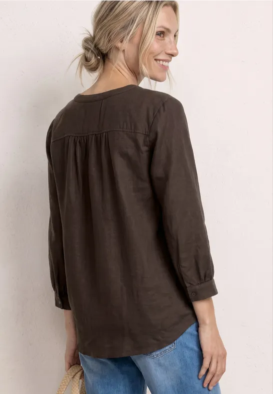 Rückansicht einer Frau in brauner Bluse und Jeans vor hellem Hintergrund.