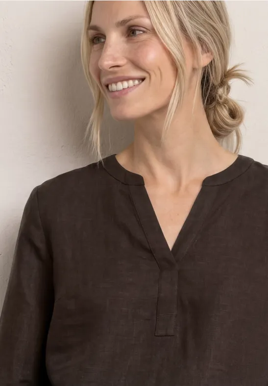 Person mit verschwommenem Gesicht trägt braunes V-Ausschnitt-Oberteil vor hellem Hintergrund.