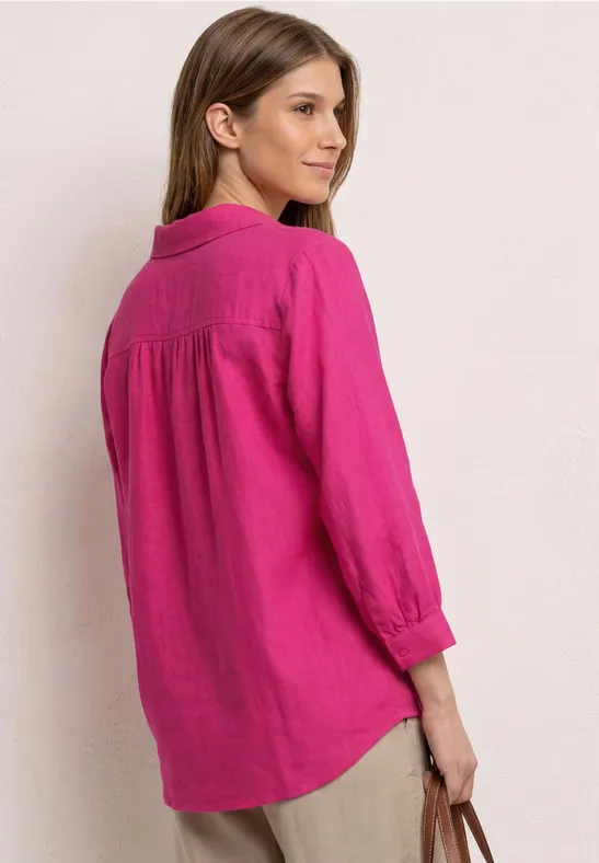 Vrouw van achteren in losse roze linnen blouse met 3/4-mouwen, ze houdt een lichte tas vast.